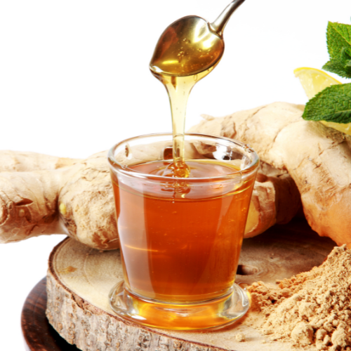 a spoon drizzling honey into a cup of ginger tea with ginger roots in the background