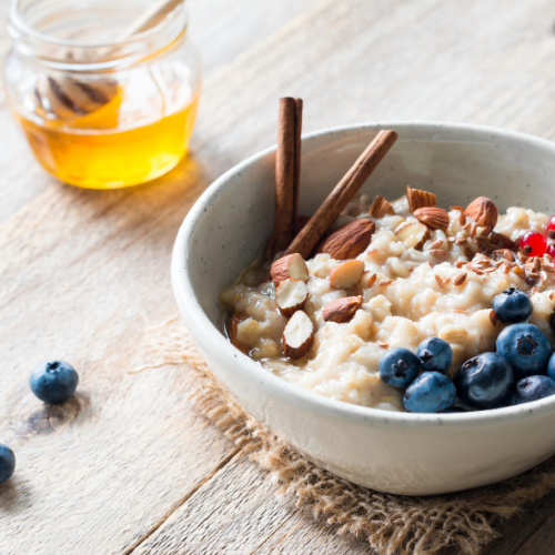 a cup of honey next to a bowl of oatmeal with walnuts, strawberries, cinnamon, and blueberries