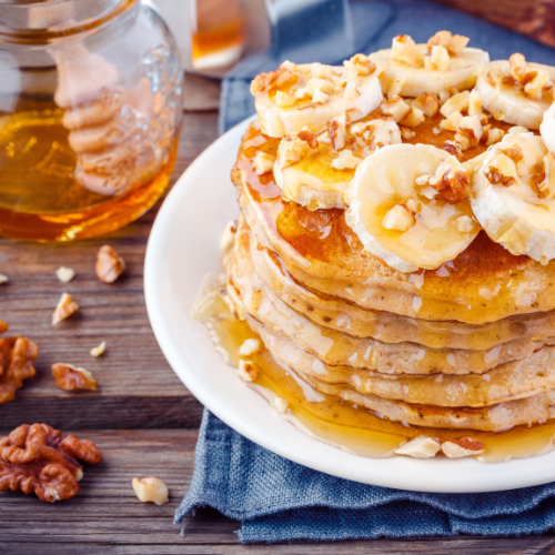 a cup of honey next to a stack of banana nut pancakes that is drizzled in honey